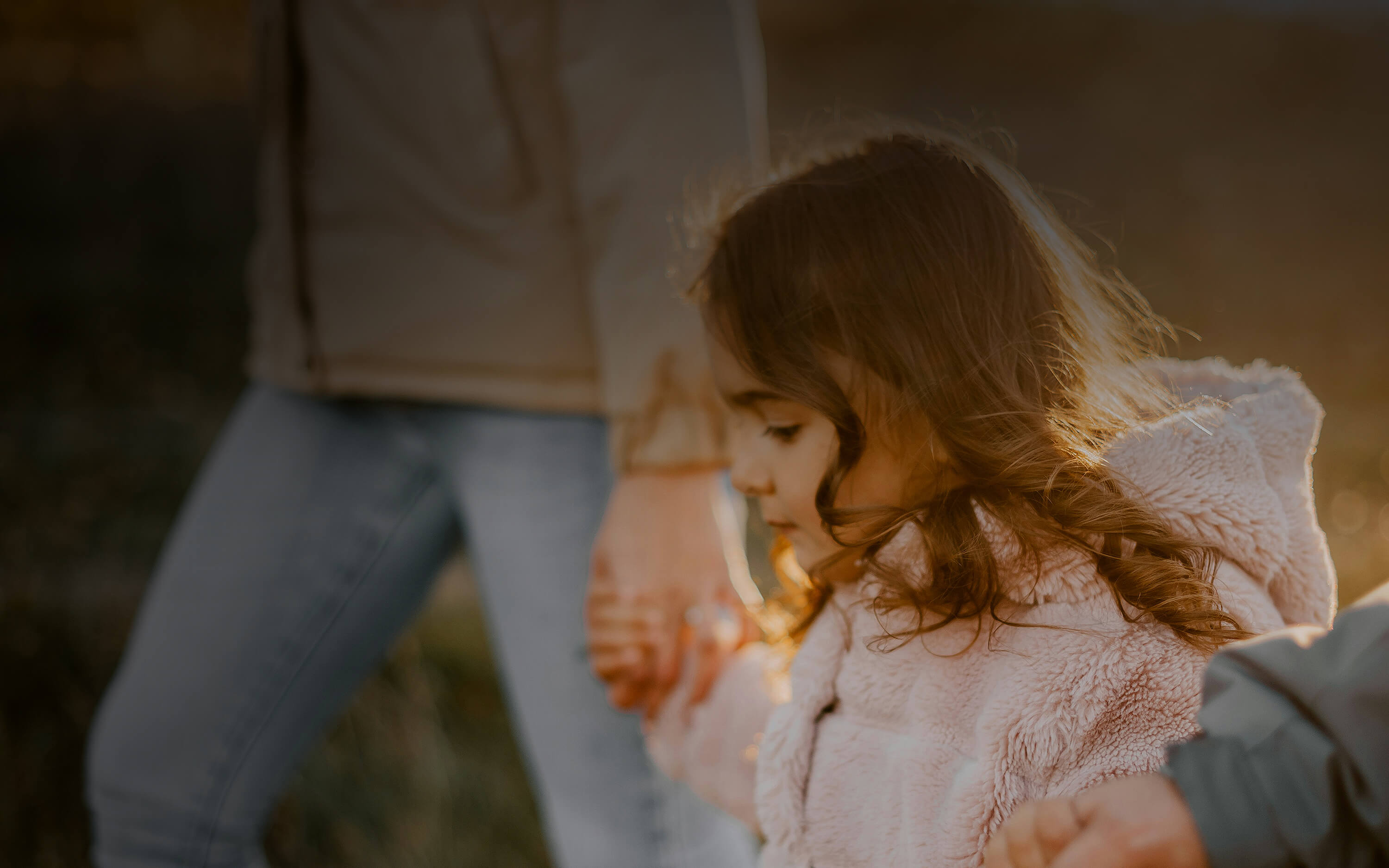 Young girl walking and holding the hands of two adults