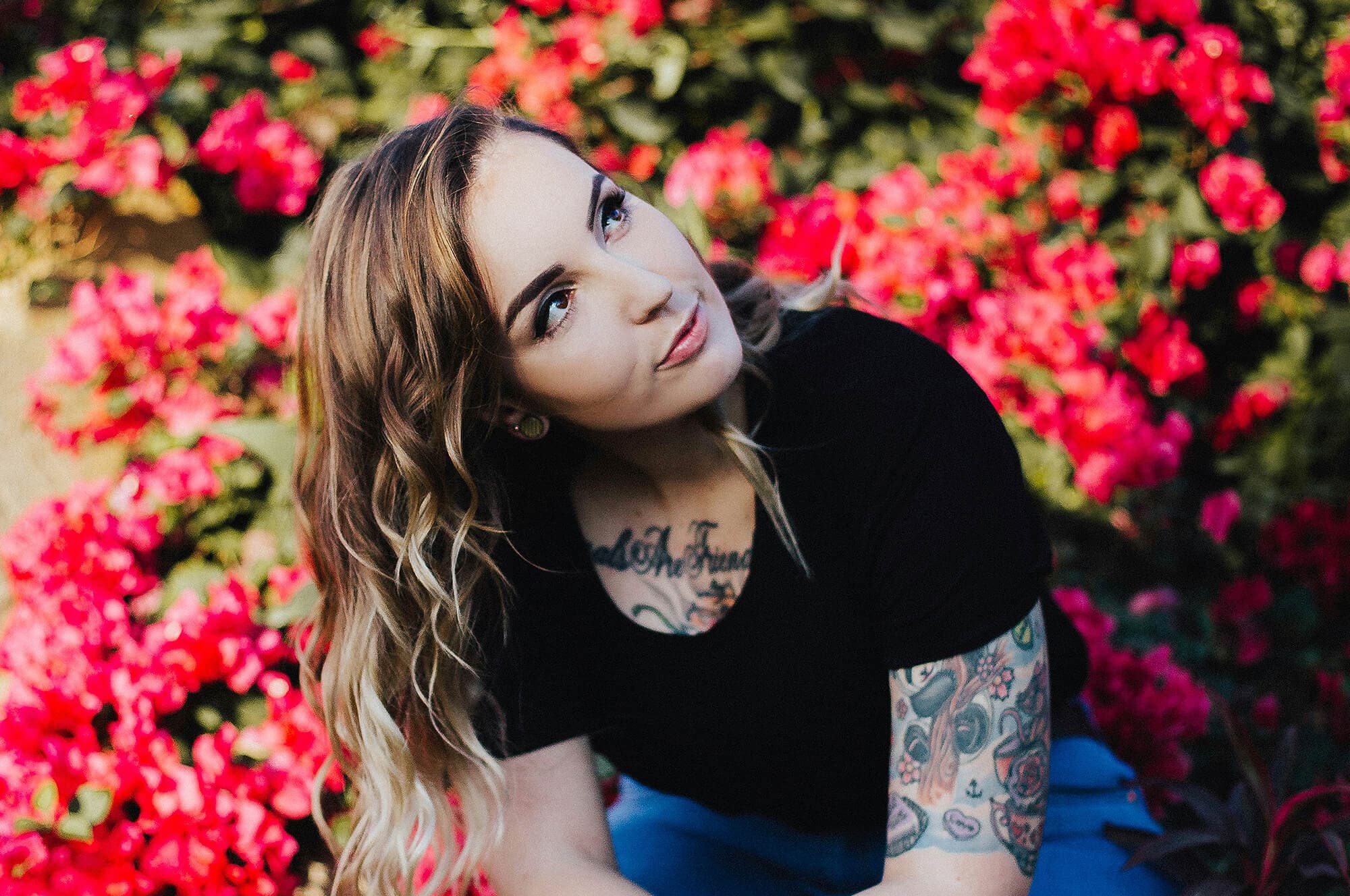 Woman with tattoos smiling and looking away at flowers